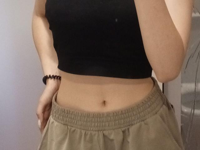 LollaKiss's midriff showing a small belly button, wearing a black crop top and beige, loose-fitting pants with a black bead bracelet on her right wrist.