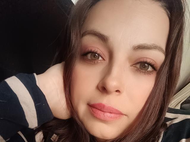 El rostro de Seher, ojos marrones, lápiz labial rosa, labios rosados ligeramente entreabiertos, cabello marrón oscuro, piel clara, camisa a rayas negras y blancas, mano detrás de la cabeza, luz suave, maquillaje sutil..