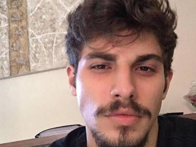 SexyMachine69 has a serious face, dark brown wavy hair, and a small mustache. He's wearing a black shirt, looking straight at the camera with a neutral expression.
