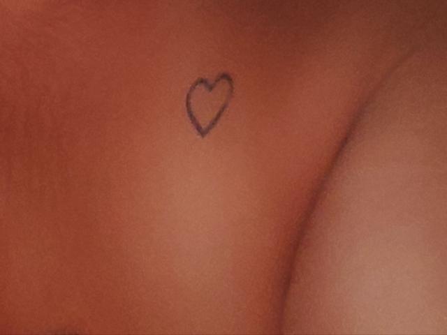 Line2323's tan skin has a small, black, outline heart tattoo on their right side, near the upper arm. The skin has a warm, slightly red tone.