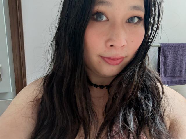 DiamondShadows has long, wet black hair, blue eyes, pink lips, and a black choker. She's looking at the camera with a slight smile, showing her tits.