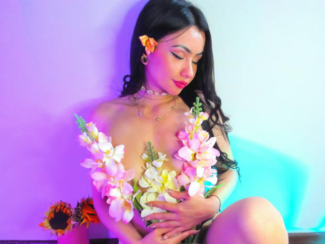 KattRouse with long black hair, pink flower in hair, holding pink and white flowers covering her tits, wearing a choker, sitting, blue and purple light, sunflower in background.