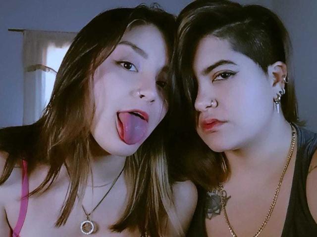 ViolletAndSussan with long brown hair sticking out tongue, and Sussan with short brown hair, nose ring, and earrings, both with necklaces, in a selfie.