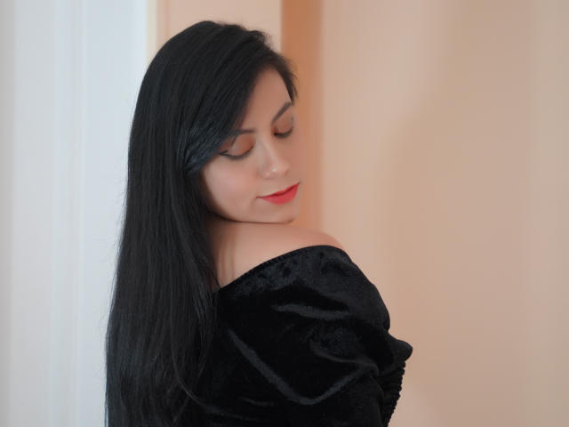 LunaFontana with long black hair, closed eyes, and red lipstick, wearing a black velvet off-shoulder top, looking slightly down and to the side. Soft, pale skin.