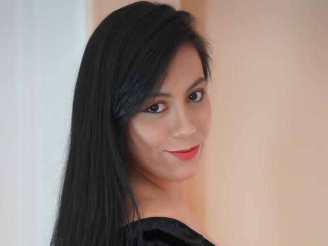 LunaFontana with black hair, brown eyes, and red lipstick, smiling at the camera, showing her cute face and black off-shoulder top. Her ass is not visible.