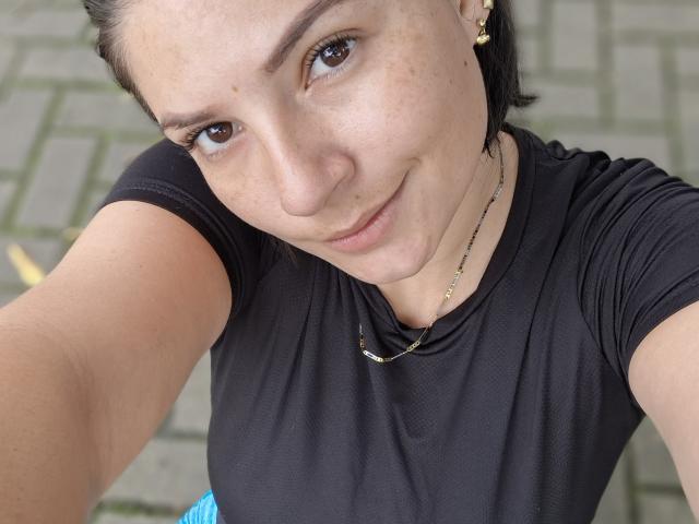 KatherineToro has light skin, brown eyes, and a slight smile. She's wearing a black shirt, gold earrings, and a necklace, with her dark hair pulled back.