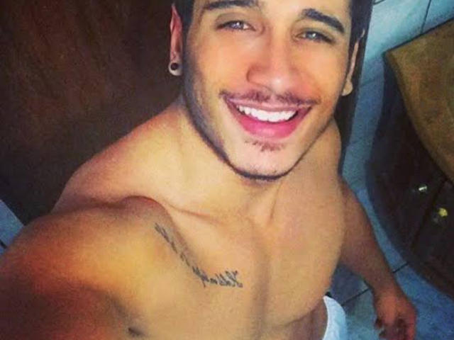 SexyMachine69 is shirtless, smiling, with a mustache, small goatee, and a tattoo on his right shoulder. He's holding a white towel, has dark hair, and is wearing ear gauges.