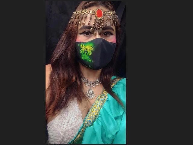 DaliaDubey with brown hair, wearing a turquoise sari, gold jewelry, black face mask with green floral design, and a jeweled headpiece, has medium tits, and dark eyes.