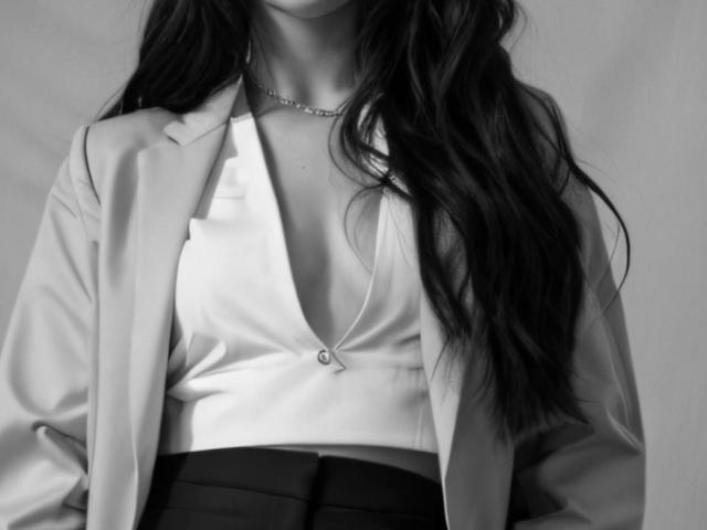 InkedFaye a dévoilé sa poitrine avec un décolleté plongeant, portant une chemise blanche à boutons et une veste ouverte, avec de longs cheveux ondulés et un collier délicat, photo en noir et blanc..