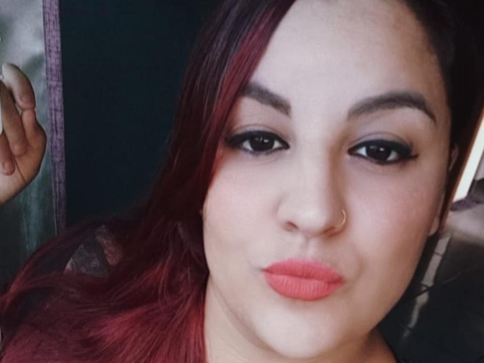 CrissieL has red hair, a nose ring, and coral lipstick. Her eyebrows are thick and she's wearing black eyeliner. Her pouty lips are slightly up. Her hand is near her face.