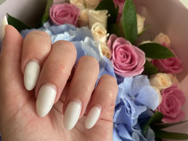 AlicePrings' hand with long, white, almond-shaped nails holding pink and white roses with blue hydrangeas, green leaves, and cream roses. Her skin is fair, nails are glossy.