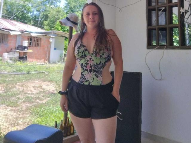 CelesteStorm with long brown hair, medium tits in a floral, deep-v, one-piece, wearing black shorts, standing, right hand in pocket, inside, next to a black speaker and wall mirror.