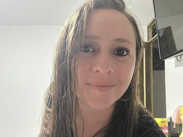 CelesteStorm with wet brown hair, small nose, and subtle smile, wearing black shirt, has small tits, and light skin, looking directly at camera, in a well-lit room.