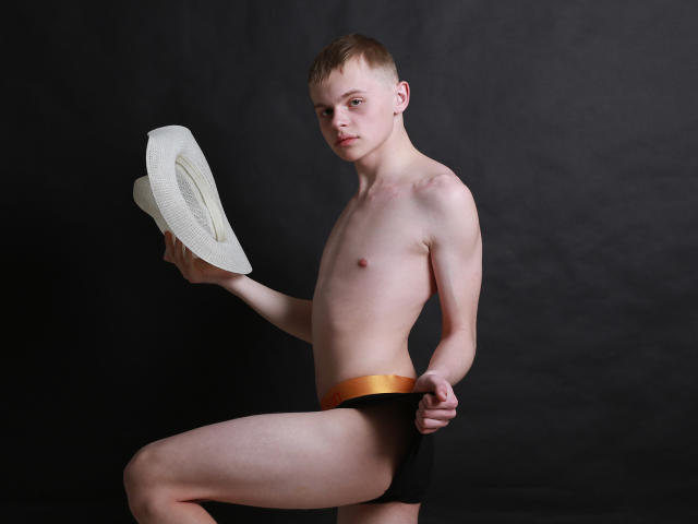 HarleyQuinXO, skinny dude with short brown hair, holding white cowboy hat, wearing black and gold briefs, standing, showing his ass, dark background, looking at camera, serious expression.
