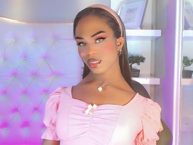Darlingsweety with brown skin, long straight hair, pink headband, pink makeup, pink dress with puffed sleeves, small white flower, necklace, smiling, pink and purple light.