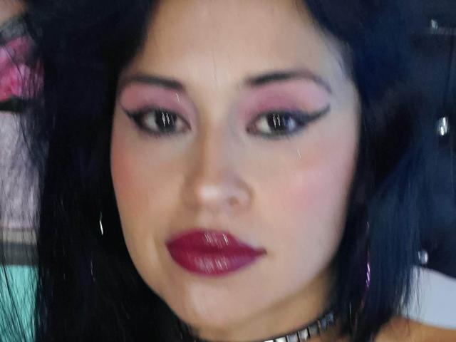 Apasion has glossy pink eyeshadow, thick black eyeliner, and shiny red lipstick. She's crying with a tear on her right cheek, and has black hair.