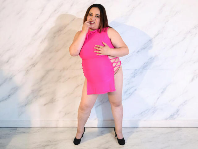 KhloeThomson, chubby with pale skin, brown hair, in a hot pink dress with side cutouts, black heels, standing, hand on chin, smiling, showing her ass, cute.