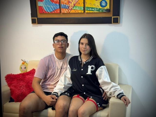 BellaThorSexUnlimit, a chubby dude with glasses, and BellaThorSexUnlimit, a cute chick with long brown hair, sitting on a couch, wearing a black and white varsity jacket.