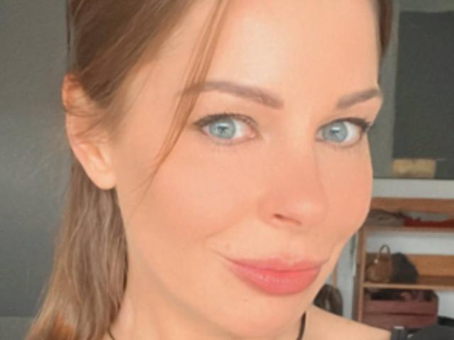 MiaXHoney has blue eyes, light brown hair in a ponytail, and pink lipstick with a subtle smile. Her eyebrows are well-defined. Her skin is fair.