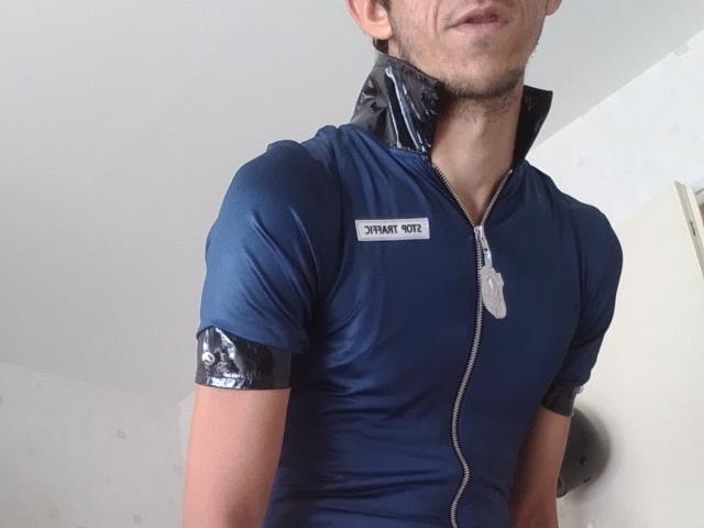 Bricebd in a tight blue shirt with black vinyl sleeves, zip-up front, and dog tags. Shirt outlines Bricebd's chest, showing a slight bulge. Bricebd's face is partially visible.