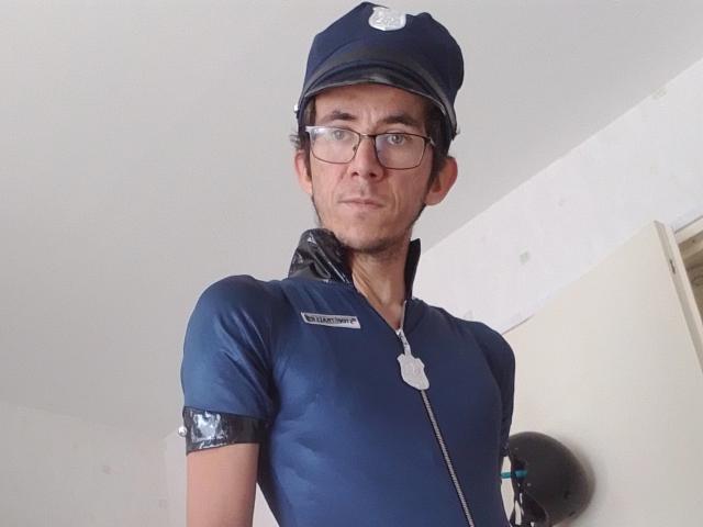 Bricebd is wearing a blue police-style outfit with a cap, glasses, and a dog tag. He has a slim build and a slight smile.