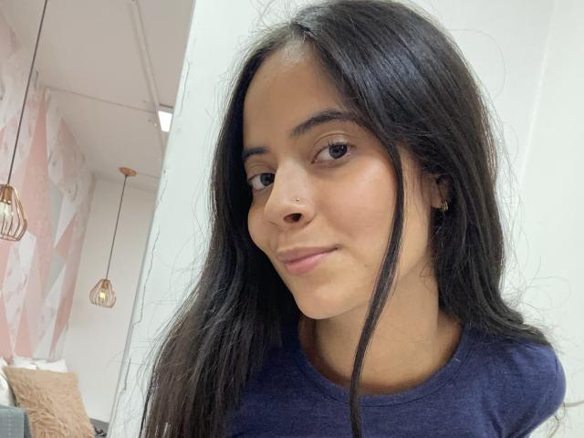 TamaraPeach tem cabelos pretos longos, um piercing no nariz e está vestindo uma camisa azul escura. Ela está sorrindo levemente, com olhos castanhos e um tom de pele marrom claro..