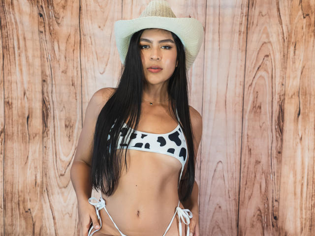SamanthaEva69 with long black hair, wearing a white and black cow print bikini and a beige cowboy hat, standing with hands on hips, showing her tits and ass.
