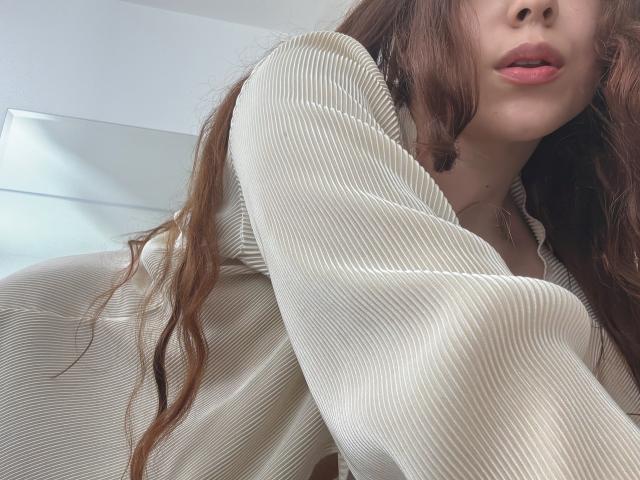 AmberlStha with long brown hair, wearing a ribbed beige shirt, showing her pouty pink lips and her small, barely visible tits. Her hand is near her chest.