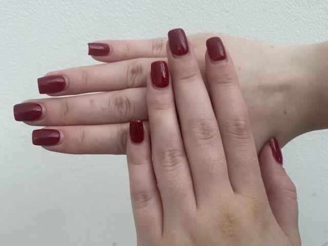 Las manos de Khori, con uñas de un rojo oscuro y brillante, dedos ligeramente curvados y piel pálida, están superpuestas, mostrando senos cuidadosamente arreglados y brillantes..