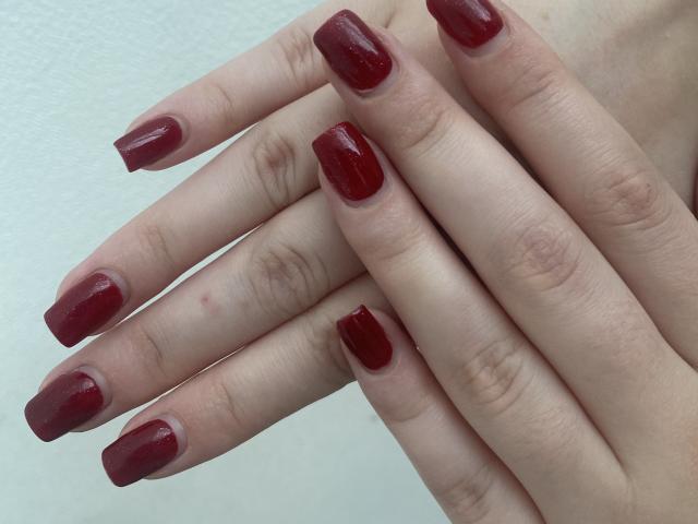 Khori's hands with shiny, red-painted nails, fingers slightly curled, showing off a fresh manicure. Her skin is pale, and the nails are well-trimmed with a glossy finish.