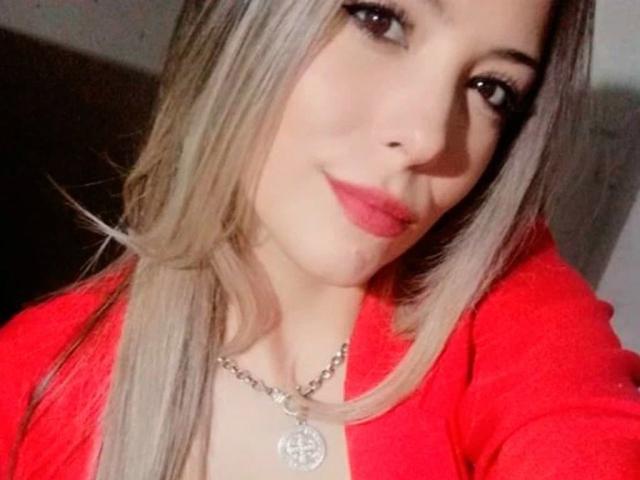 EvaBcn-hot with blonde hair, red lipstick, and a red sweater, wearing a silver necklace with a circular pendant, smiling at the camera. Boobs partially visible.