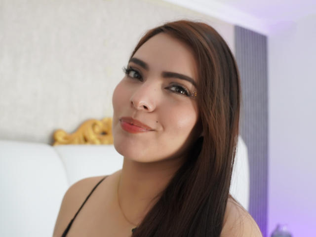 ReginaFiore has dark brown hair, a cute nose ring, and a subtle smile. She's wearing black eyeliner and a thin black top, with a gentle, sexy look.