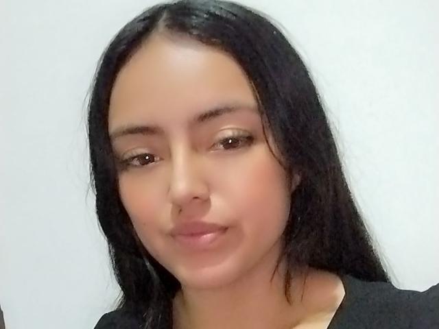 AilynRoss has medium brown skin, long black hair, and a subtle smile. She's wearing a black top and has a cute, relaxed face with small brown eyes.