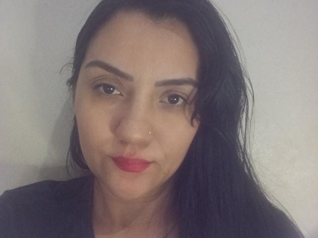 PatriciaLinda has dark brown eyes, black hair, red lipstick, and a small nose piercing. She's wearing a black shirt, looking straight at the camera with a slight smile.