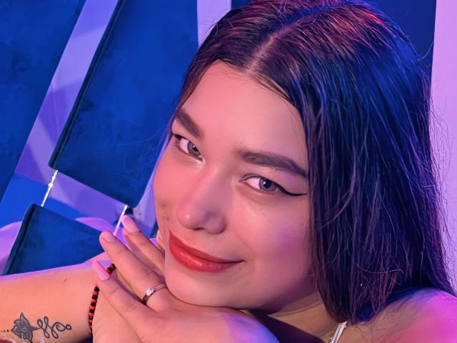 SeleneI has wet brown hair, red lipstick, and a tattoo on her left shoulder. She's smiling with her hand on her chin, eyes lined with black eyeliner.