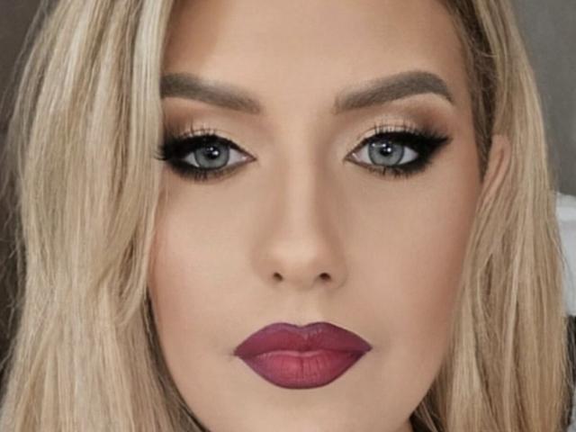 OndinaNoir's face, showing blue eyes with thick black eyeliner, blonde hair, full pinkish-red lipstick, and subtle eyeshadow, looking straight at the camera.