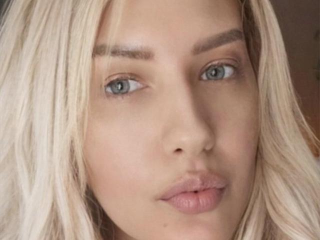 OndinaNoir has blonde hair, blue eyes, and pink lips with a neutral expression. Her eyebrows are slightly raised. Her skin is fair and her face is centered in the shot.