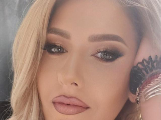 OndinaNoir's face, blonde hair, blue eyes, thick eyebrows, dark eyeliner, pink lipstick, subtle tattoo on her ear, hand with silver bracelets, soft skin, slight smile, sexy.