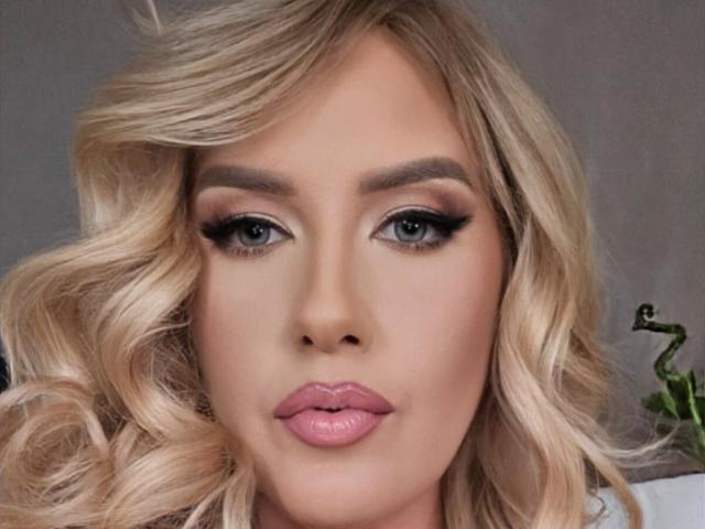 OndinaNoir has blonde, wavy hair, blue eyes, and pink lips with black eyeliner and mascara. Her face is centered, showing a smooth, fair complexion.