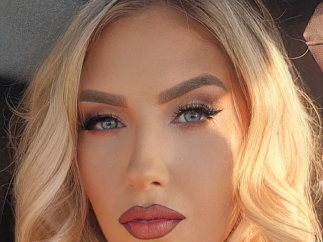OndinaNoir has blonde wavy hair, blue eyes with thick black eyelashes, and full pinkish-brown lips. Her eyebrows are perfectly shaped and she's looking straight at the camera.