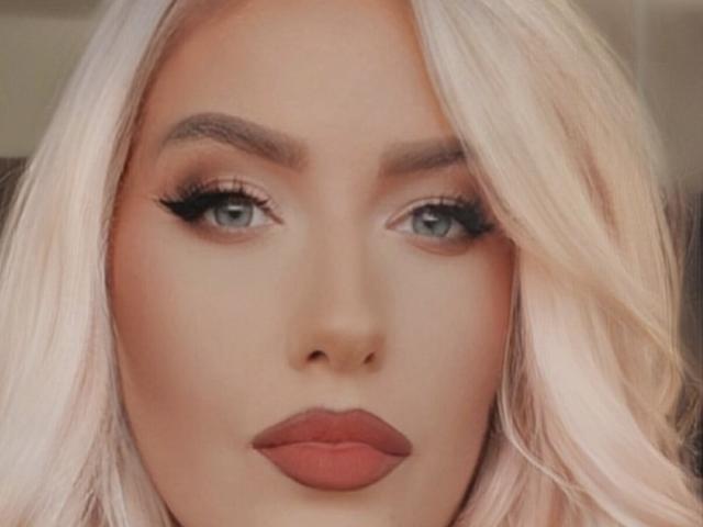 OndinaNoir's face with pinkish blonde hair, blue eyes, thick eyebrows, long black eyelashes, and red lipstick. Her ass is not visible. Her tits are not visible.