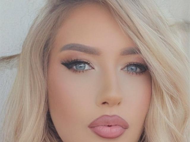 OndinaNoir has blonde hair, blue eyes, thick eyebrows, long eyelashes, and pink lips. Her makeup is glamorous, with a focus on her eyes and full lips.