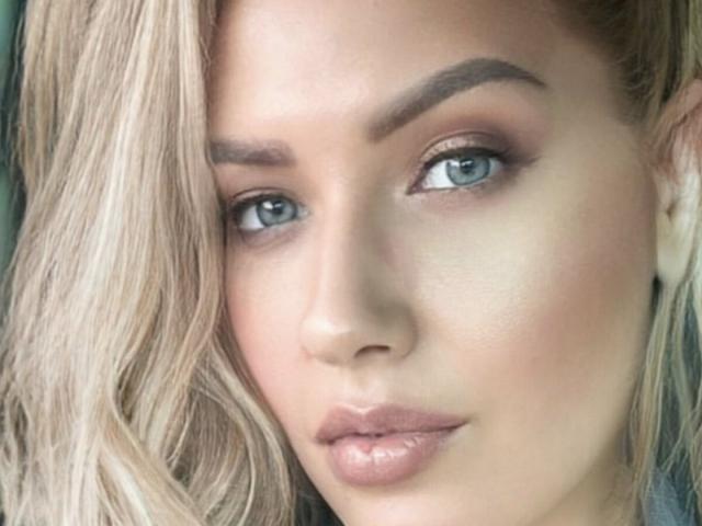OndinaNoir's face, showing blue eyes, blonde hair, groomed eyebrows, and shiny pink lips. Her skin is smooth with a subtle, natural glow. She looks directly at the camera.