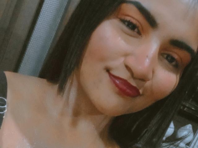 SusanaDiaz has a cute smile with red lipstick, dark eyebrows, and straight black hair, showing her shiny bare shoulders and a small nose ring. She's looking at the camera.