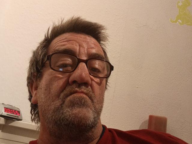 Habeckle has a graying, spiky beard, glasses, and a serious face. He's wearing a red shirt with a black collar, and a device is on the left.