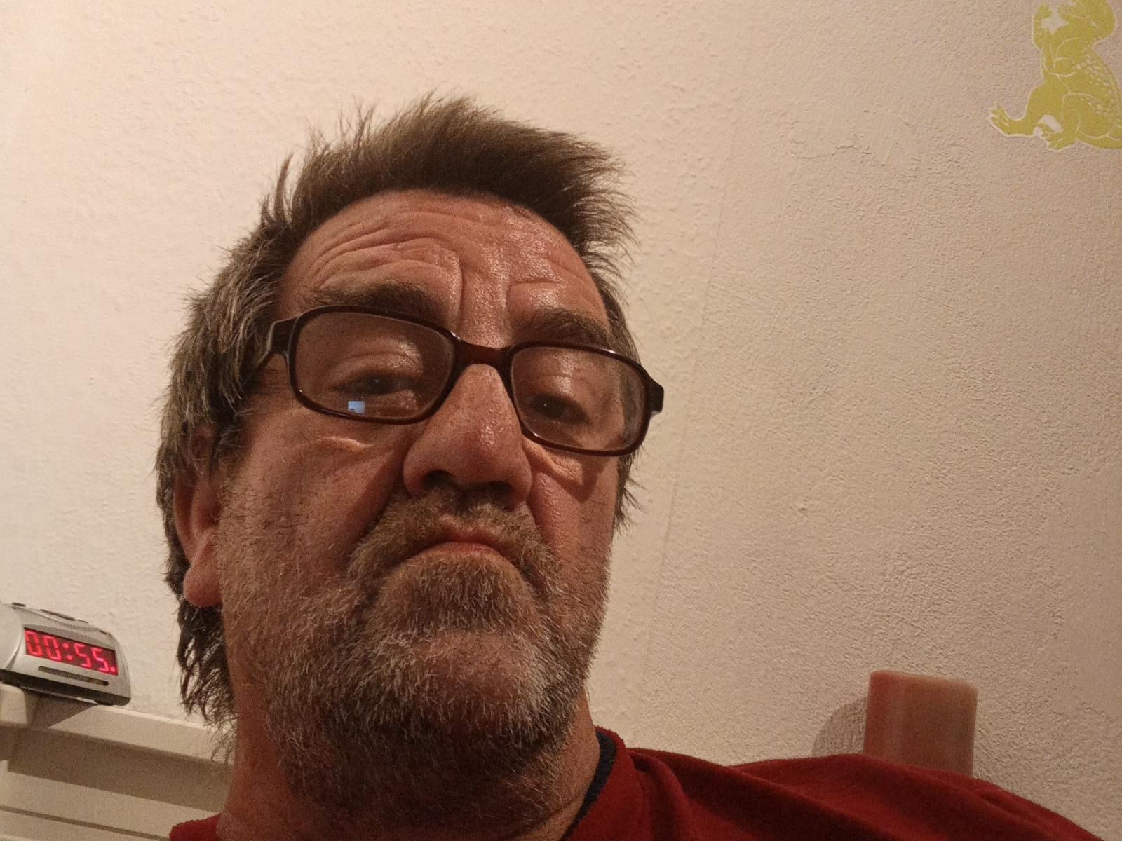 Habeckle has a graying, spiky beard, glasses, and a serious face. He's wearing a red shirt with a black collar, and a device is on the left.