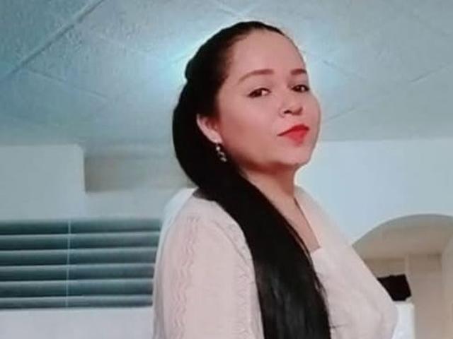 DulceHunny with long black hair, wearing a white lace top, has red lipstick and earrings, looking slightly to the side with a subtle smile.