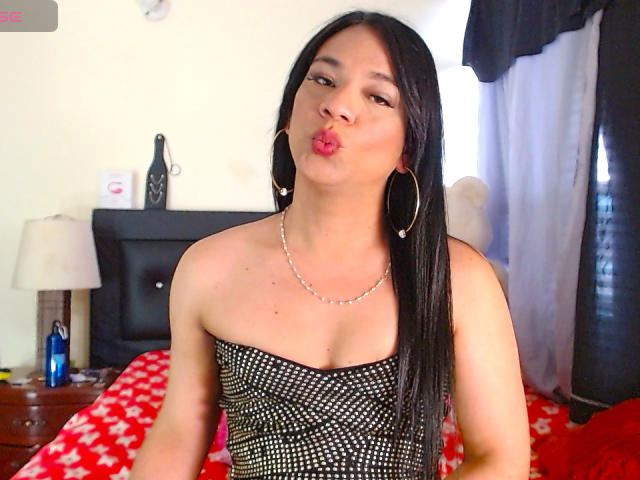 CatalineHot with long black hair, pouty pink lips, wearing a strapless black and white dotted top, large hoop earrings, and a silver necklace, kissing air.
