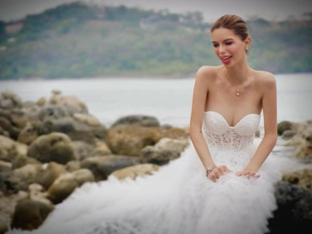 HotCumAdriana69x with small tits in a white, lace, strapless wedding dress, sitting on rocks by the water, smiling, brown hair in a bun, wearing a necklace.