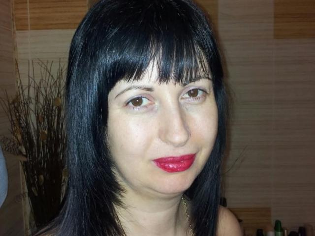 SweetMichele has black straight hair, bangs, brown eyes, and bright red lipstick. She's smiling slightly with a fair skin tone, showing a cute and attractive face.